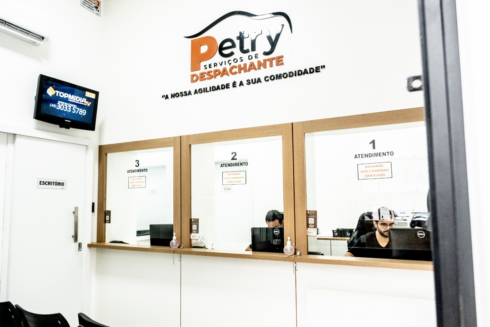 Sala de atendimento presencial da Petry com 3 guichês numerados sob o logo na parede